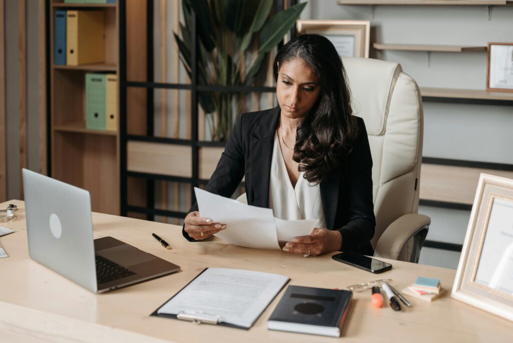Business woman focused on paperwork at office desk, reviewing documents.